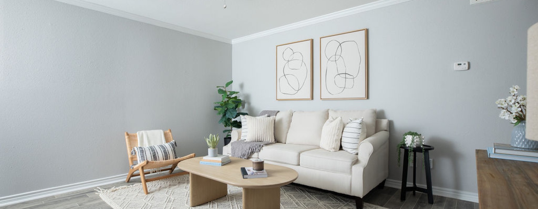Modern living room featuring a beige sofa, accent chair, wood coffee table, indoor plants, and minimalist wall art.